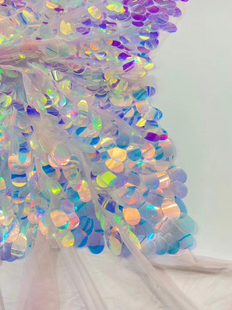 May include: White iridescent sequins on a sheer mesh fabric. The sequins are round and have a holographic finish.