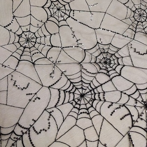 Può includere: Tessuto in pizzo nero a forma di ragnatela con paillettes argentate. Il tessuto ha un design delicato e intricato, perfetto per l'artigianato o la decorazione.