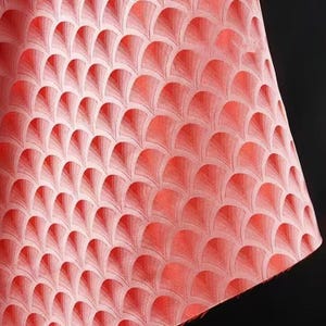 Könnte beinhalten: Ein korallenfarbener Stoff mit einem sich wiederholenden fächerförmigen Muster. Das Design weist einen Farbverlauf auf, mit helleren Koralltönen an der Spitze jedes Fächers und dunkleren Tönen an der Basis. Der Stoff wird wahrscheinlich für Heimdekoration oder Mode verwendet.