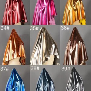 May include: Nine samples of metallic fabric in different colors, including red, pink, gold, orange, silver, bronze, blue, dark blue, and gray. Each sample is draped over a mannequin head.
