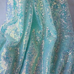 May include: A close-up of iridescent turquoise blue fabric with sequins. The fabric is soft and shimmery, with a subtle sheen.