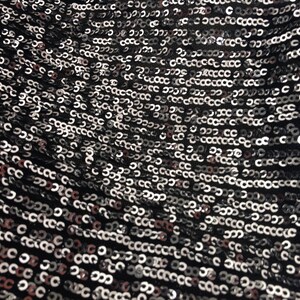 May include: Close-up of a black fabric covered in silver sequins. The sequins are arranged in a repeating pattern.