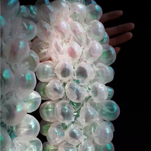 May include: Close-up of a cluster of translucent, bubble-like forms with iridescent highlights. The forms are clustered together, creating a textured, organic appearance. The background is black, emphasizing the glowing quality of the forms.