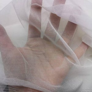 May include: Close-up of sheer white fabric with a fine mesh texture. The fabric is layered, creating depth and highlighting the transparency. The material appears soft and delicate, ideal for crafting or decorative purposes.