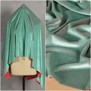 May include: A draped piece of fabric with a shimmering mint green surface and a contrasting solid coral red underside. The fabric is displayed on a mannequin torso marked with the number 84, showing a soft, reflective texture with deep folds.