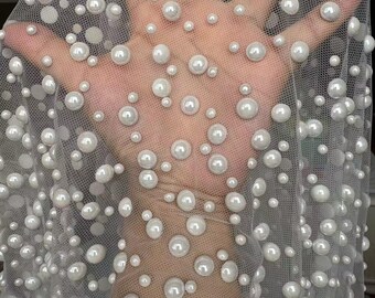May include: White tulle fabric with white pearl embellishments. The pearls are of varying sizes and are scattered randomly across the fabric.