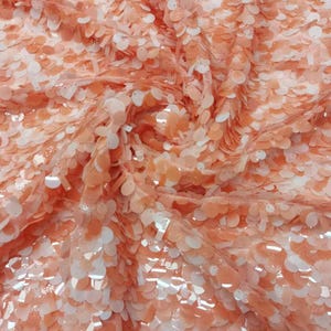 May include: Peach-colored fabric with a textured pattern of overlapping sequins. The sequins are translucent and have a slight shimmer.