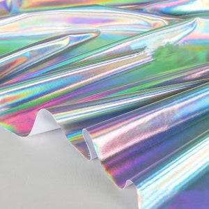 May include: Close-up of iridescent fabric with a holographic finish. The fabric is folded and shows a rainbow of colors.