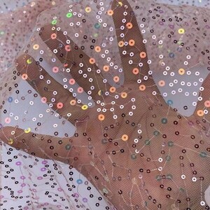 May include: Pink sheer fabric with iridescent sequins in a scattered pattern. The sequins are small and round, and they create a shimmering effect.