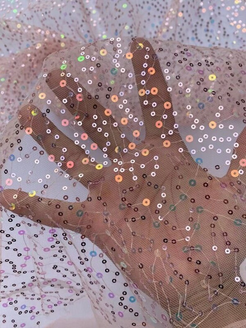 May include: Pink sheer fabric with iridescent sequins in a scattered pattern. The sequins are small and round, and they create a shimmering effect.