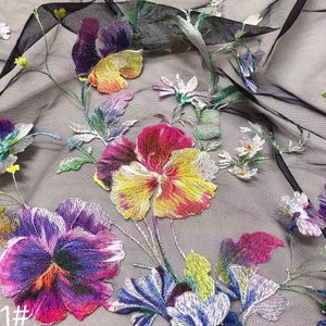 May include: Black sheer fabric with embroidered floral designs. The flowers are in shades of purple, pink, yellow, and green. The fabric has a delicate, airy feel.