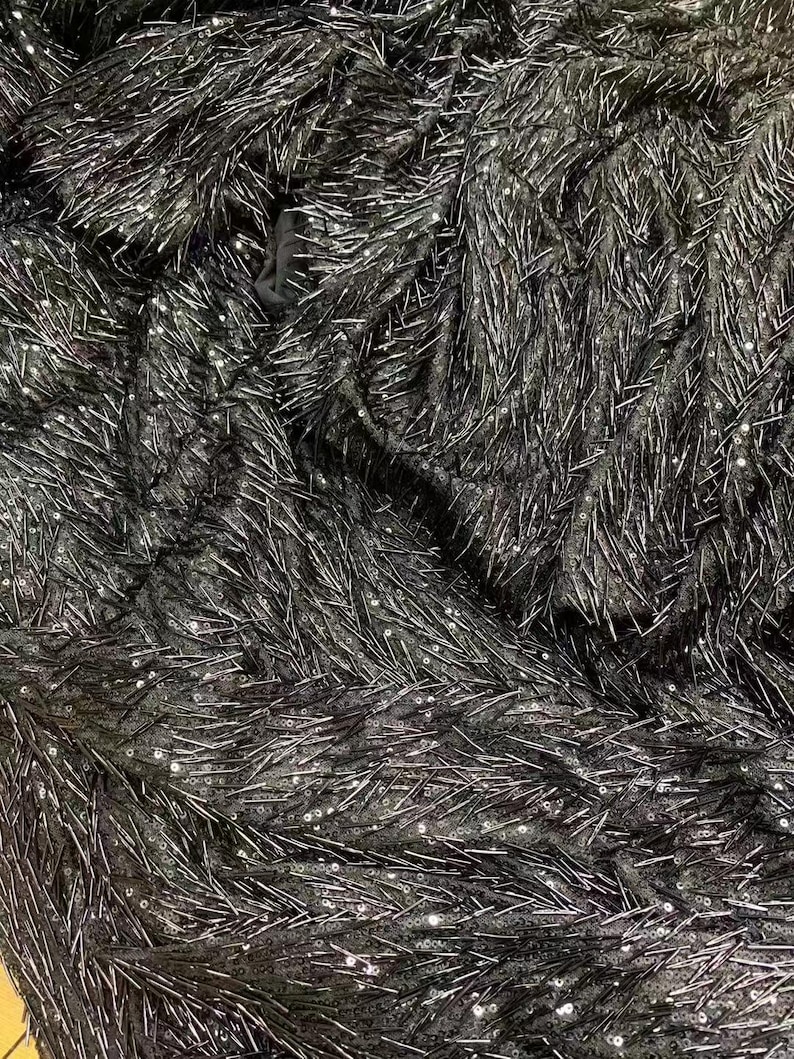 K&ouml;nnte beinhalten: Schwarzer Stoff mit einer strukturierten Oberfl&auml;che, die mit kleinen, silbernen Pailletten bedeckt ist. Die Pailletten sind in einem zuf&auml;lligen Muster angeordnet und erzeugen einen schimmernden Effekt.