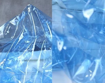 May include: Abstract image featuring translucent, light blue plastic material. The material is crumpled and folded, creating a textured, layered effect. The folds and creases catch the light, creating highlights and shadows.
