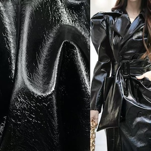 Peut inclure: Un trench-coat noir brillant, avec une ceinture à la taille et de larges revers. Le manteau a une finition brillante, semblable à du cuir verni, et présente un design croisé. L'image montre la texture du matériau et la silhouette générale du manteau.
