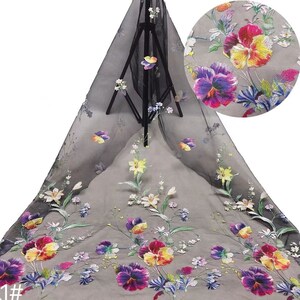 May include: Black sheer fabric with an embroidered floral design. The flowers are colourful with shades of purple, yellow, red, and pink. The fabric has a delicate, airy feel.