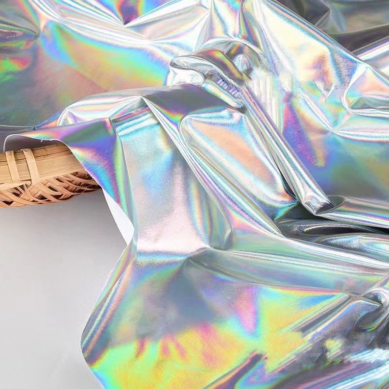 May include: Silver iridescent fabric with a holographic finish. The fabric is folded and draped over a woven basket.