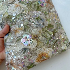 May include: A beige fabric with a floral pattern and iridescent sequins. The fabric is sheer and has a delicate texture.