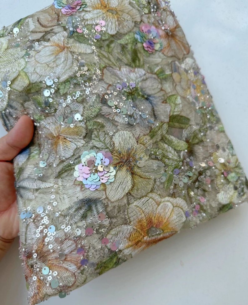 May include: A beige fabric with a floral pattern and iridescent sequins. The fabric is sheer and has a delicate texture.
