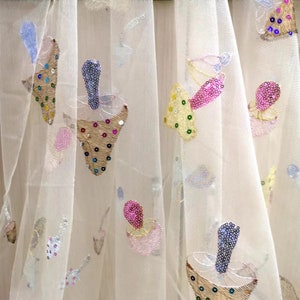 Puede incluir: Tela blanca transparente con setas bordadas de colores y otros diseños. La tela está decorada con lentejuelas y cuentas.