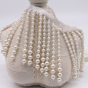 May include: White pearl trim with a beaded fringe. The trim is displayed on a fabric covered mannequin form.