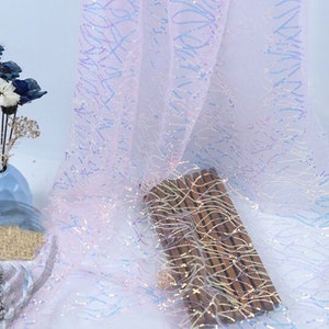 May include: White iridescent fabric with a subtle pattern of blue and pink lines. The fabric has a shimmery, sparkly finish.