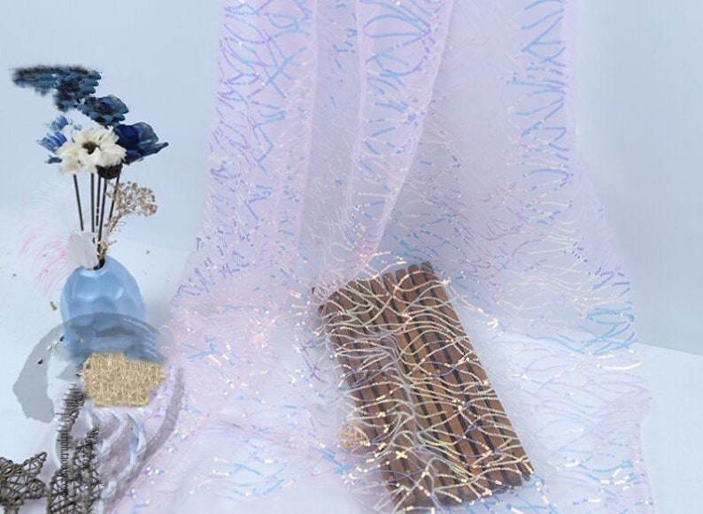 May include: White iridescent fabric with a subtle pattern of blue and pink lines. The fabric has a shimmery, sparkly finish.