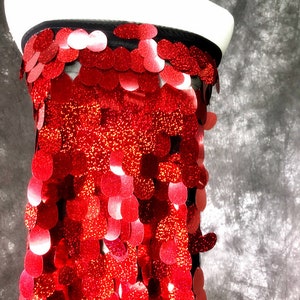 May include: Red sequin fabric with a circular pattern. The sequins are shiny and have a slight iridescent effect.
