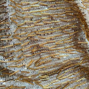 May include: A sheer fabric featuring a dense pattern of small, round, iridescent white sequins and elongated, metallic gold-toned bugle beads arranged in a scattered, multi-directional layout across the entire surface of the material.