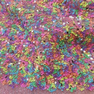 May include: A close-up of a pink fabric with a rainbow sequin design. The sequins are arranged in a swirling pattern.