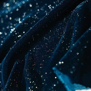 Könnte beinhalten: Nahaufnahme eines dunkelblauen Stoffes mit einem funkelnden, glitzernden Effekt. Der Stoff ist drapiert und erzeugt Falten und Schatten. Der Glitzer ist über die Oberfläche verstreut und erzeugt den Eindruck von Sternen am Nachthimmel.