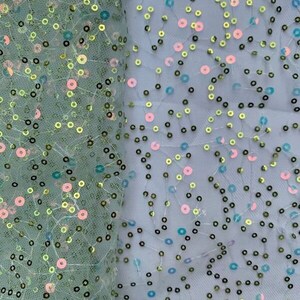 May include: Green, blue, and pink iridescent sequins on a sheer mesh fabric. The sequins are scattered randomly across the fabric.