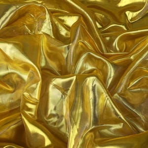 Op de afbeelding: Een metallic gouden stof met een hoogglanzende afwerking, voorzien van diepe plooien en complexe drapages die een ingewikkeld patroon van licht en schaduw over het oppervlak creëren, wat de reflecterende kwaliteit van het materiaal benadrukt.