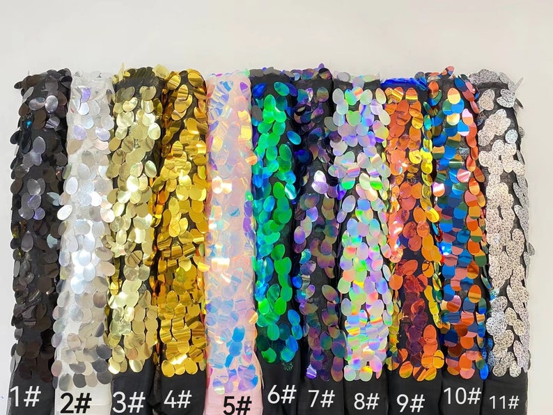 May include: Eleven different colors of sequin fabric swatches. The swatches are arranged horizontally from left to right. The colors are black, silver, gold, iridescent pink, green, iridescent blue, iridescent purple, red, blue, silver, and black.
