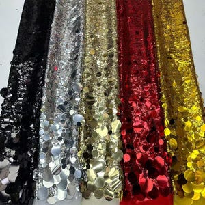 May include: Five fabric swatches featuring large, round sequins. The swatches are black, silver, gold, red, and gold. The sequins are iridescent and reflect light.