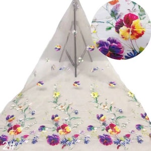 May include: White sheer fabric with colourful embroidered flowers. The flowers are a mix of pinks, yellows, blues, and purples. The fabric is delicate and has a soft texture.