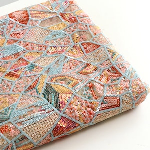 Può includere: Un tessuto blu chiaro con un motivo geometrico di paillettes in tonalità di rosa, arancio, giallo e verde.