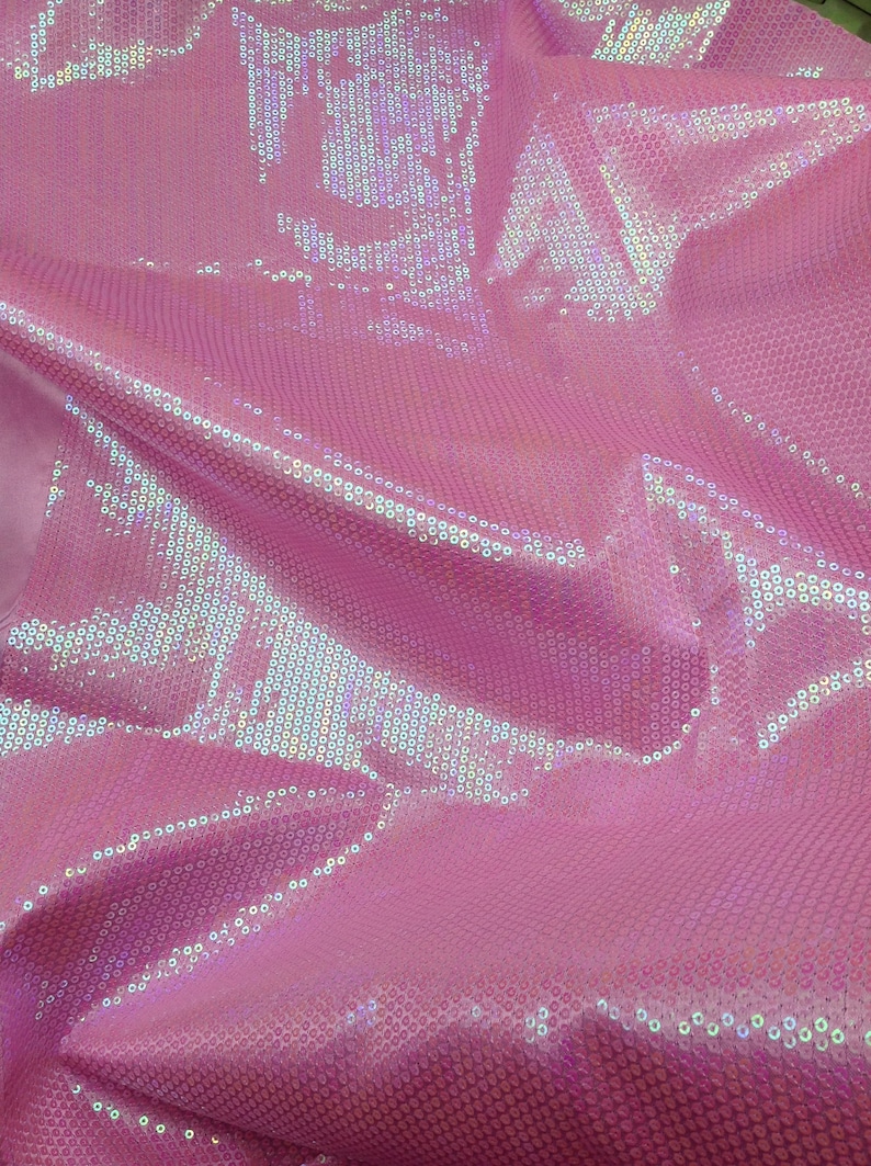 Op de afbeelding: Roze, iriserende stof met een paillettenpatroon. De pailletten zijn klein en dicht bij elkaar geplaatst, waardoor een glinsterend effect ontstaat.