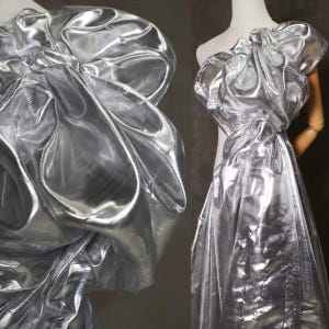 May include: Silver metallic fabric with a crinkled texture. The fabric is sheer and has a reflective surface.