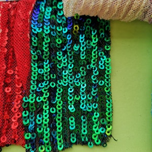 May include: A close-up of a green, blue, and black sequined fabric with a red sequined fabric to the left. The fabric is labelled with the numbers 12, 13, 14, and 15.