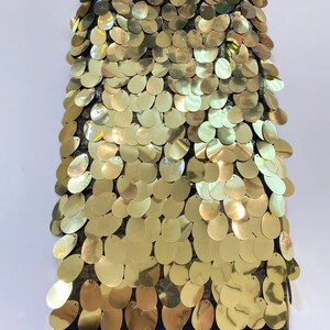 May include: Gold sequin fabric with a black mesh backing. The sequins are oval shaped and arranged in a scale pattern.