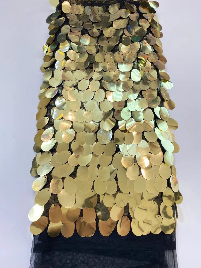 May include: Gold sequin fabric with a black mesh backing. The sequins are oval shaped and arranged in a scale pattern.