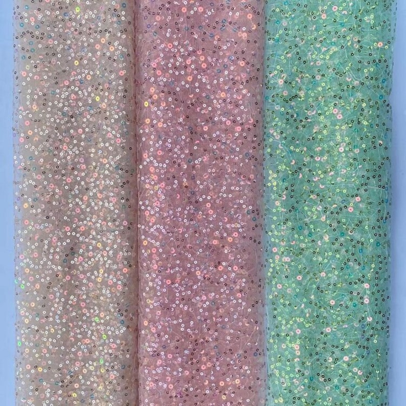 May include: Three rolls of iridescent sequin fabric in white, pink, and green. The fabric is sheer and has a delicate sparkle.