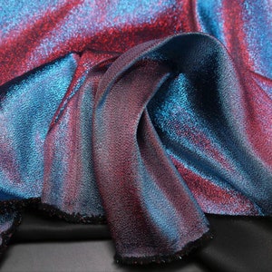 Può includere: Primo piano di un tessuto scintillante con un gradiente di blu e rosso. Il tessuto ha una texture sottile e un riflesso metallico.
