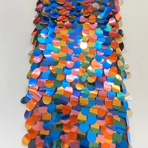 May include: A piece of iridescent fabric with a rainbow pattern of sequins. The sequins are oval shaped and are sewn onto a black mesh fabric.