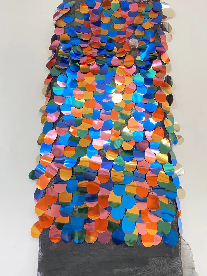 May include: A piece of iridescent fabric with a rainbow pattern of sequins. The sequins are oval shaped and are sewn onto a black mesh fabric.