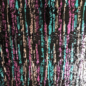 Pode incluir: Tecido preto com listras verticais de lantejoulas turquesa, rosa e dourado. O tecido tem um acabamento brilhante e iridescente.