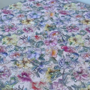 May include: A pink fabric with a floral pattern and sequins. The fabric is a sheer, lightweight material with a delicate floral design. The sequins are scattered throughout the fabric, adding a touch of sparkle.
