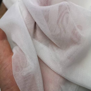 May include: Close-up of white sheer fabric. The fabric is thin and delicate, with a fine mesh weave. The light passes through the fabric, creating highlights and shadows. The fabric is soft and flowing, with a slight sheen.