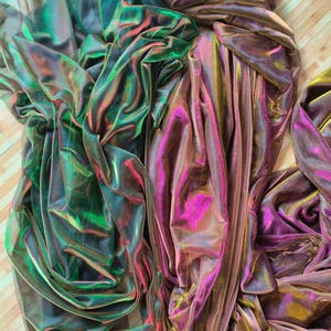 May include: Two pieces of iridescent sheer fabric draped together. The left piece displays a vibrant shift between deep green and dark purple tones. The right piece features a shimmering blend of magenta, gold, and bronze hues with a fine mesh texture.