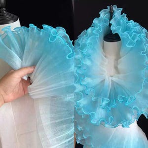 May include: A large, blue and white tulle collar with ruffled edges. The collar is made of a soft, sheer fabric and has a delicate, feminine look.